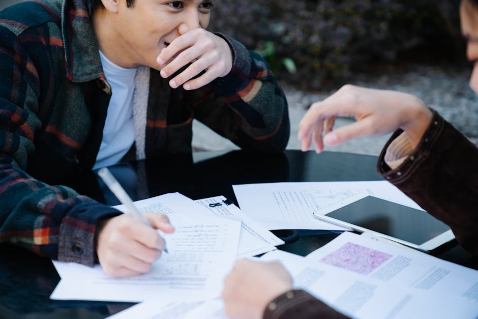 Two students sharing ideas over study papers and a tablet outdoors