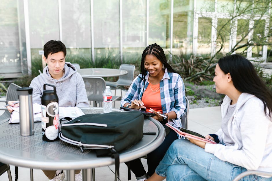 A group of diverse university students studying together outdoors, collaborating with books and tablets