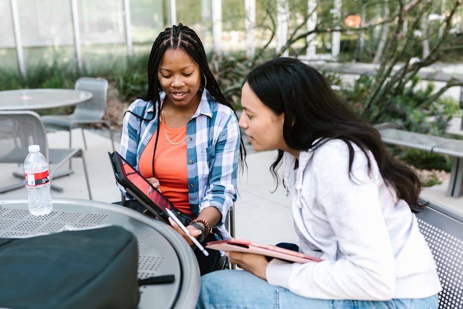 Two young women studying together using a tablet at outdoor campus seating